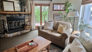 A living room with a stone fireplace, a sofa, a coffee table, and a lamp. - Aspen Cottage Ski In Ski Out 1BR at Lutsen Mtn (Lutsen)