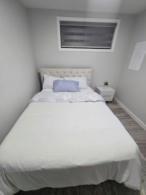 Ein Schlafzimmer mit einem Bett, einem Nachttisch, einer kleinen Topfpflanze und einem Fenster.