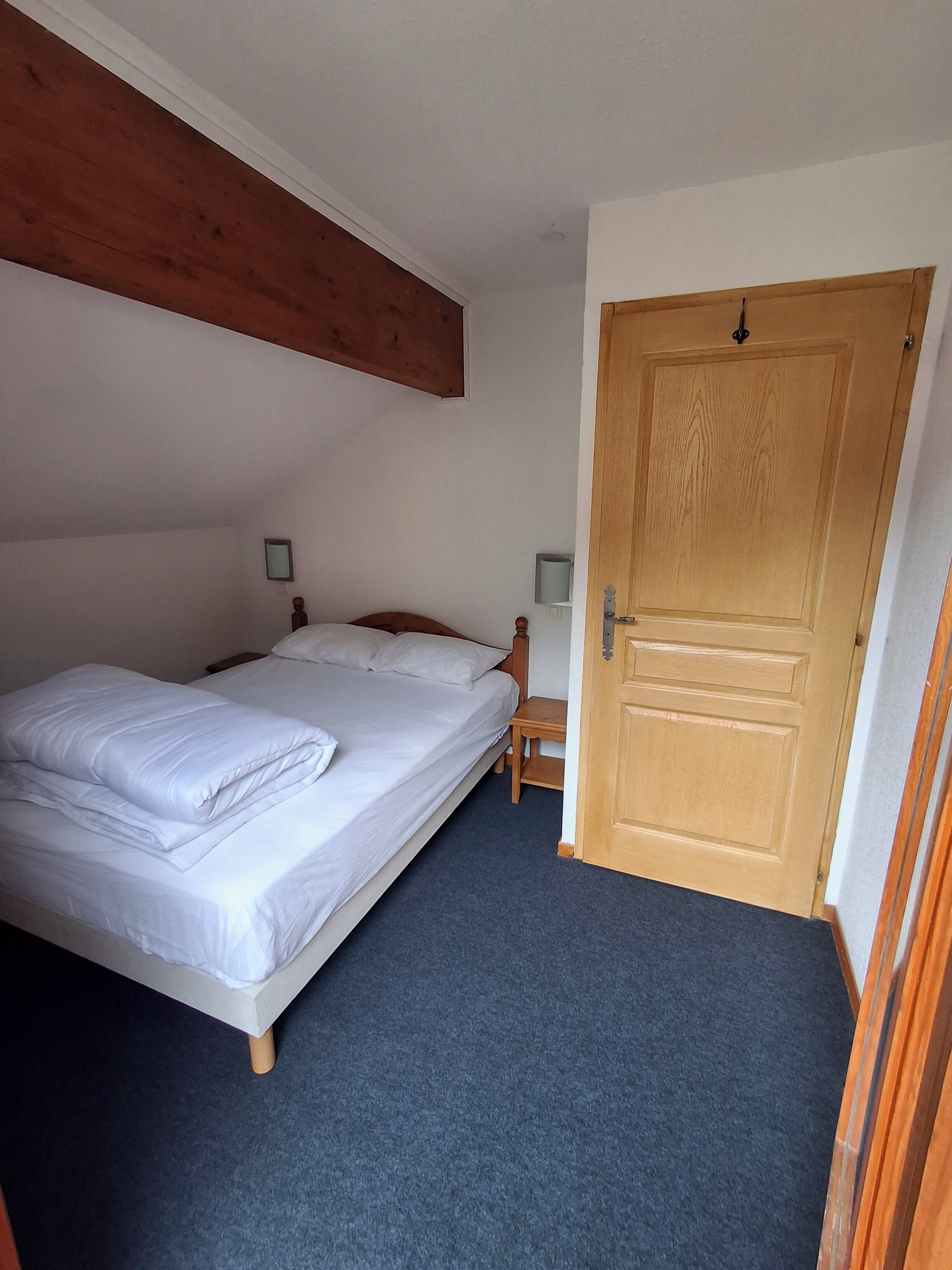 Ein Schlafzimmer mit einem Bett, einer Holztür und einem kleinen Tisch mit Stuhl.