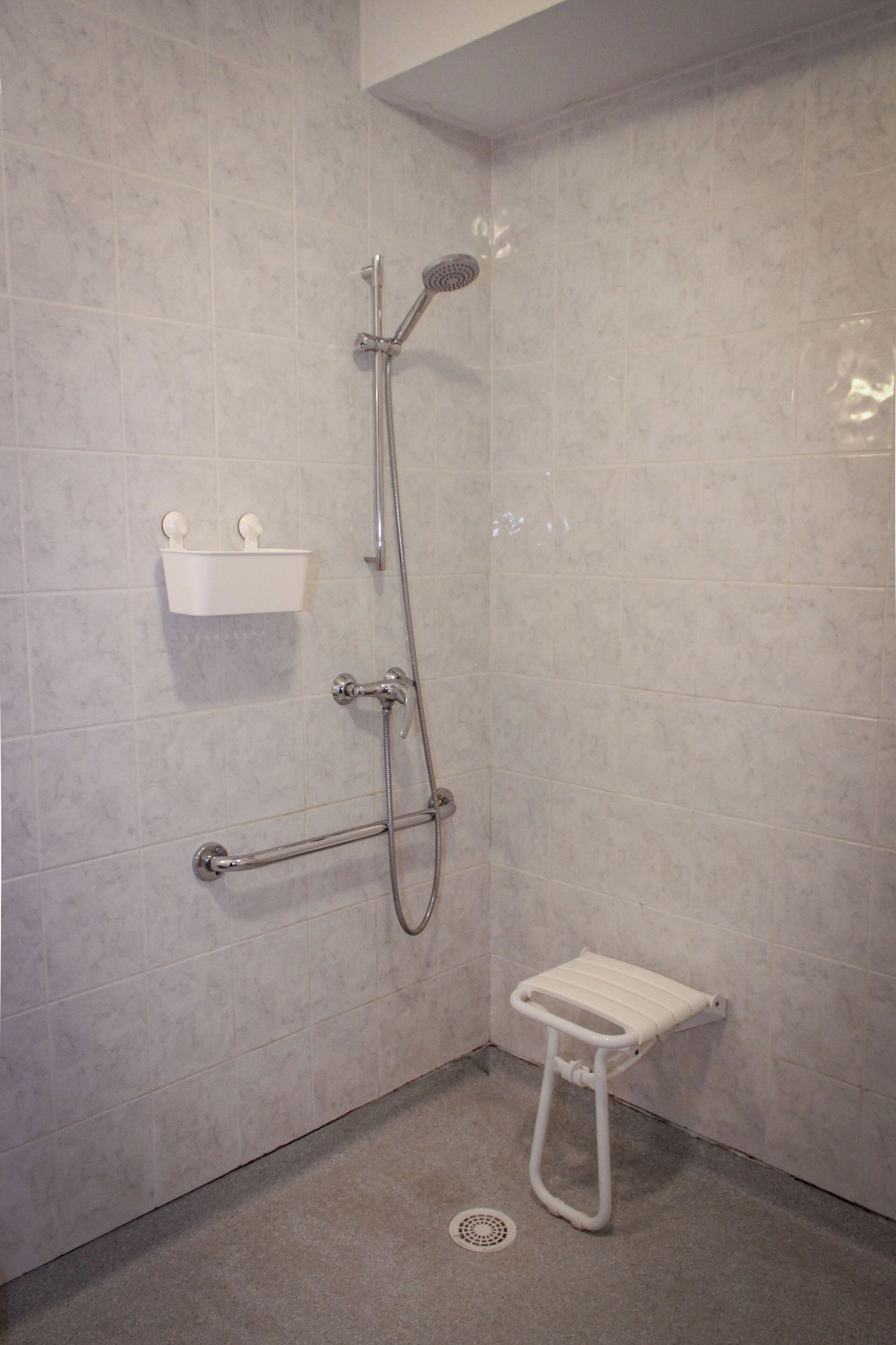 A shower with a handheld showerhead, a handheld shower attachment, and a small white step stool.