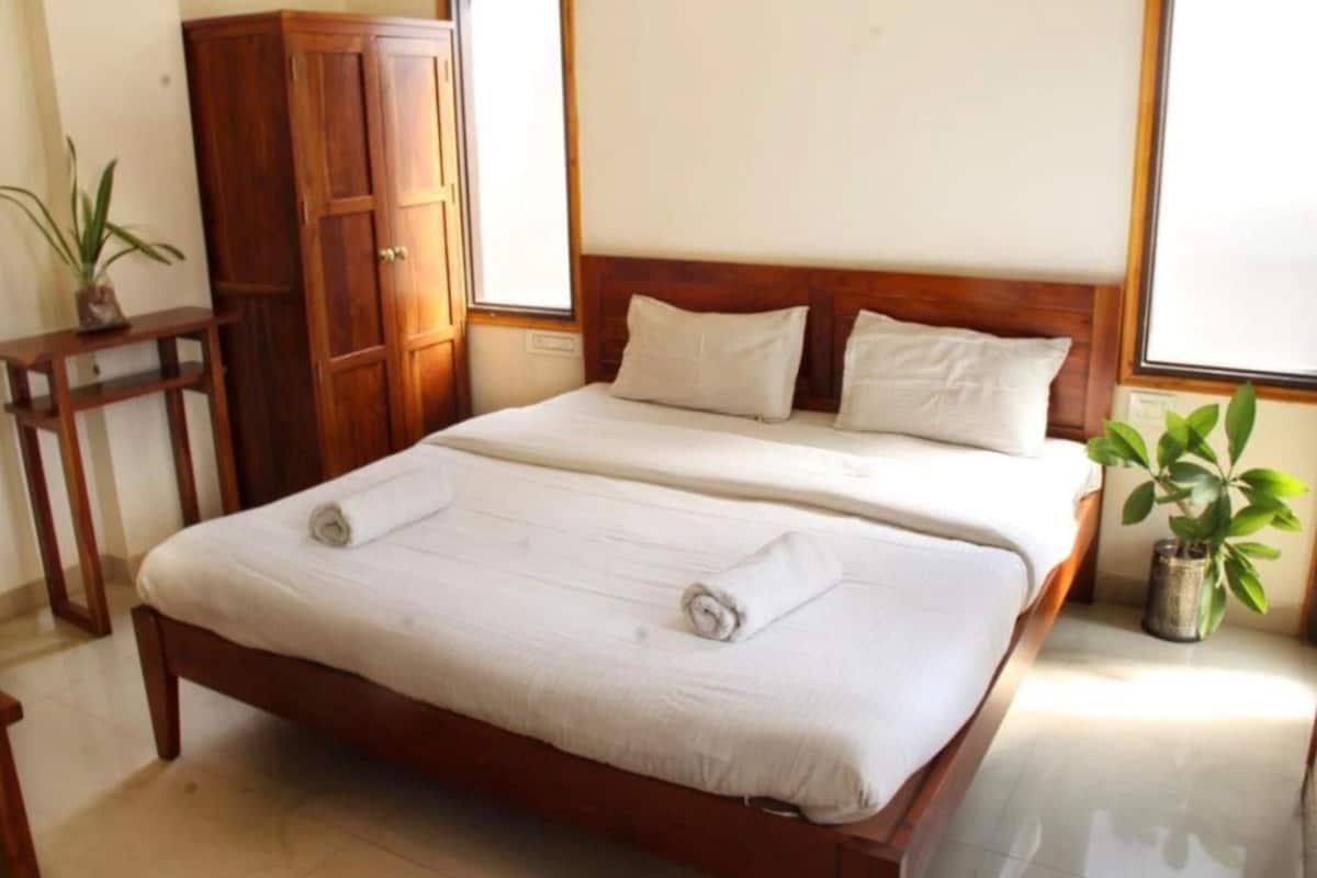 Una cama doble con sábanas blancas, cabecera de madera y dos almohadas.