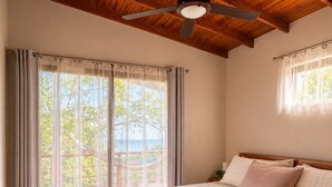 Camera da letto con un grande letto, travi in legno a soffitto, ventilatore a soffitto e vista sull'esterno.