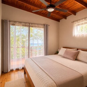 Ein Schlafzimmer mit einem großen Bett, Holzbalkendecke, Deckenventilator und Blick ins Freie.