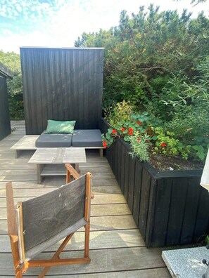Eine Holzterrasse mit integriertem Sitzbereich, einem kleinen Tisch und einem Blumenbeet mit roten Blüten.