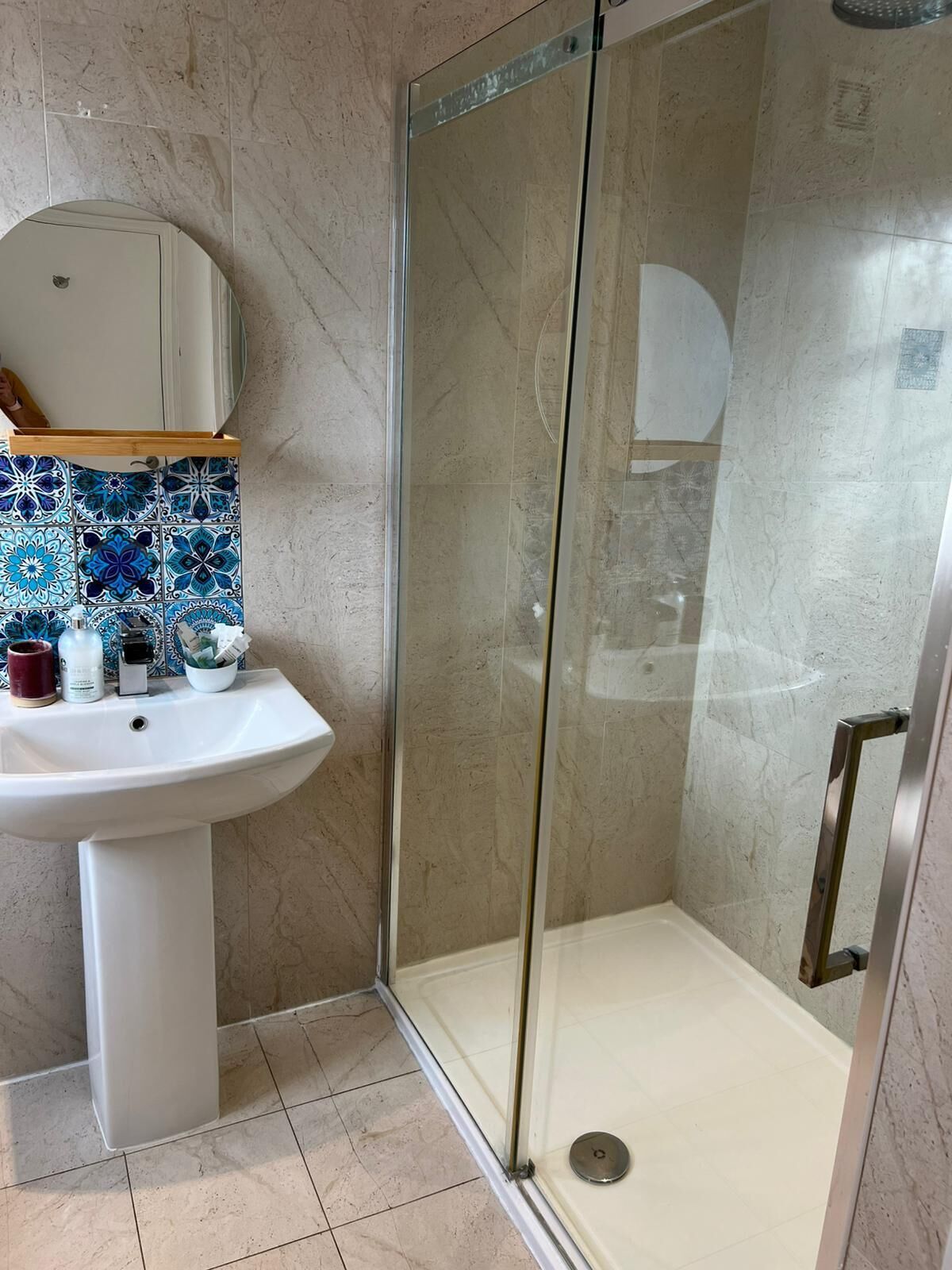 Un baño con ducha de vidrio, un lavamanos pedestal blanco y un salpicadero de azulejos.