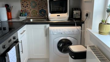 A compact kitchen with a built-in oven, a microwave, a washing machine, and a trash bin.