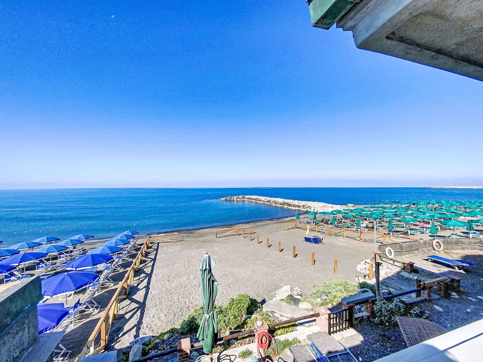 A beach with umbrellas and lounge chairs, a clear sky, and the sea.