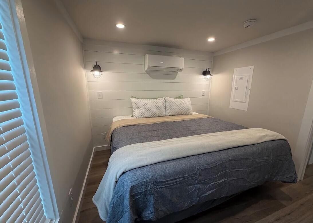 Quarto com cama, duas luzes na parede, aparelho de ar condicionado e janela com persianas.