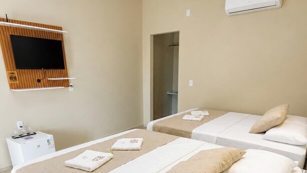 A hotel room with two beds, a TV mounted on the wall, an air conditioning unit, and a small table with a water dispenser.