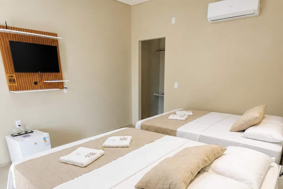 Ein Hotelzimmer mit zwei Betten, einem an der Wand montierten Fernseher, einer Klimaanlage und einem kleinen Tisch mit Wasserspender.