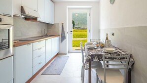 Una cucina con mobili bianchi, forno integrato e vista su un campo verde attraverso una porta aperta.