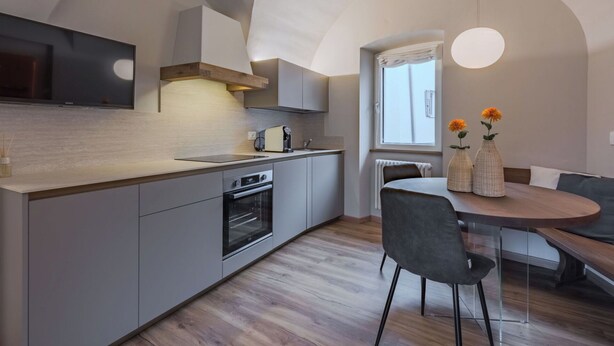 A modern kitchen with a built-in oven, a dining area with a round table and chairs, and a large window with curtains. - Cosy apartment for 6 people with WIFI, TV and balcony (Ossana)