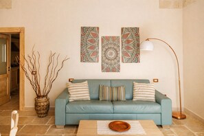 A living room with a teal sofa, patterned wall art, a vase with branches, and a floor lamp. - Villa [2 suites] 5 minutes from the sea | air conditioning | garden | BBQ | outdoor shower (Diso)