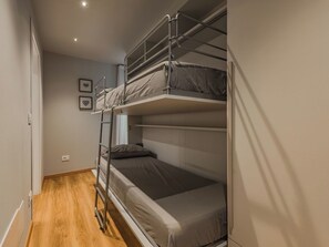 Dormitorio con literas, escalera, suelo de madera y una ventana pequeña.