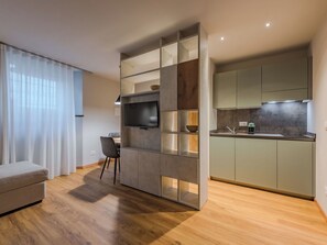Ein modernes Wohnzimmer mit Fernseher, Essbereich und einer Küche mit Einbauofen.