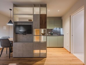 Una cocina moderna con televisor integrado, estantes de madera y una zona de comedor con sillas.