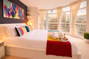 A hotel room with a large bed, a colorful abstract painting, a city view, and a window with curtains. - Chic 2BR Suite in the Heart of Toronto's Entertainment District (Toronto)