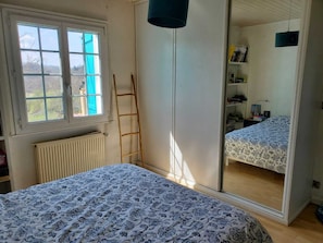 Ein Schlafzimmer mit Bett, Kleiderschrank, Heizkörper, Fenster und einer Leiter.