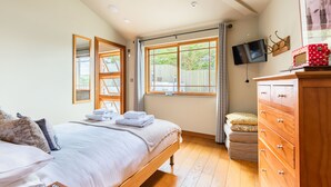 Ein Schlafzimmer mit Bett, einem Holzschrank, Fernseher und großen Fenstern.