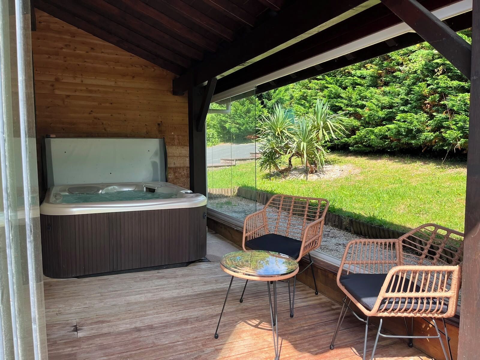 A hot tub in a wooden cabin with wicker chairs and a view of greenery.