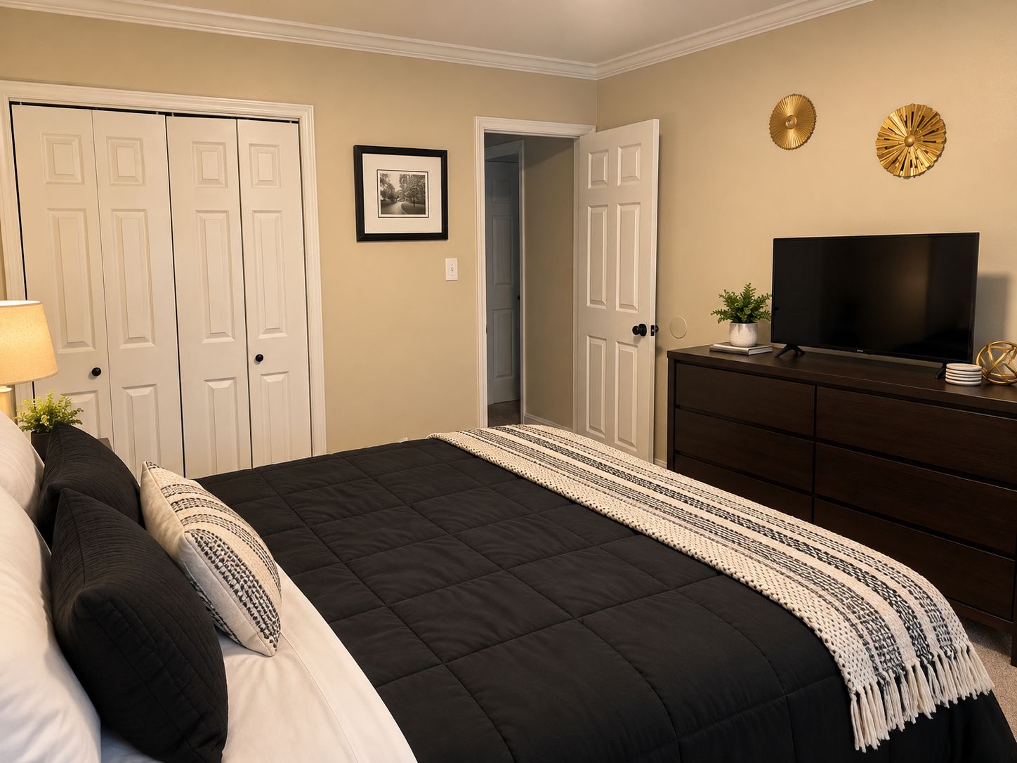 A bedroom with a bed, dresser, television, and two doors.