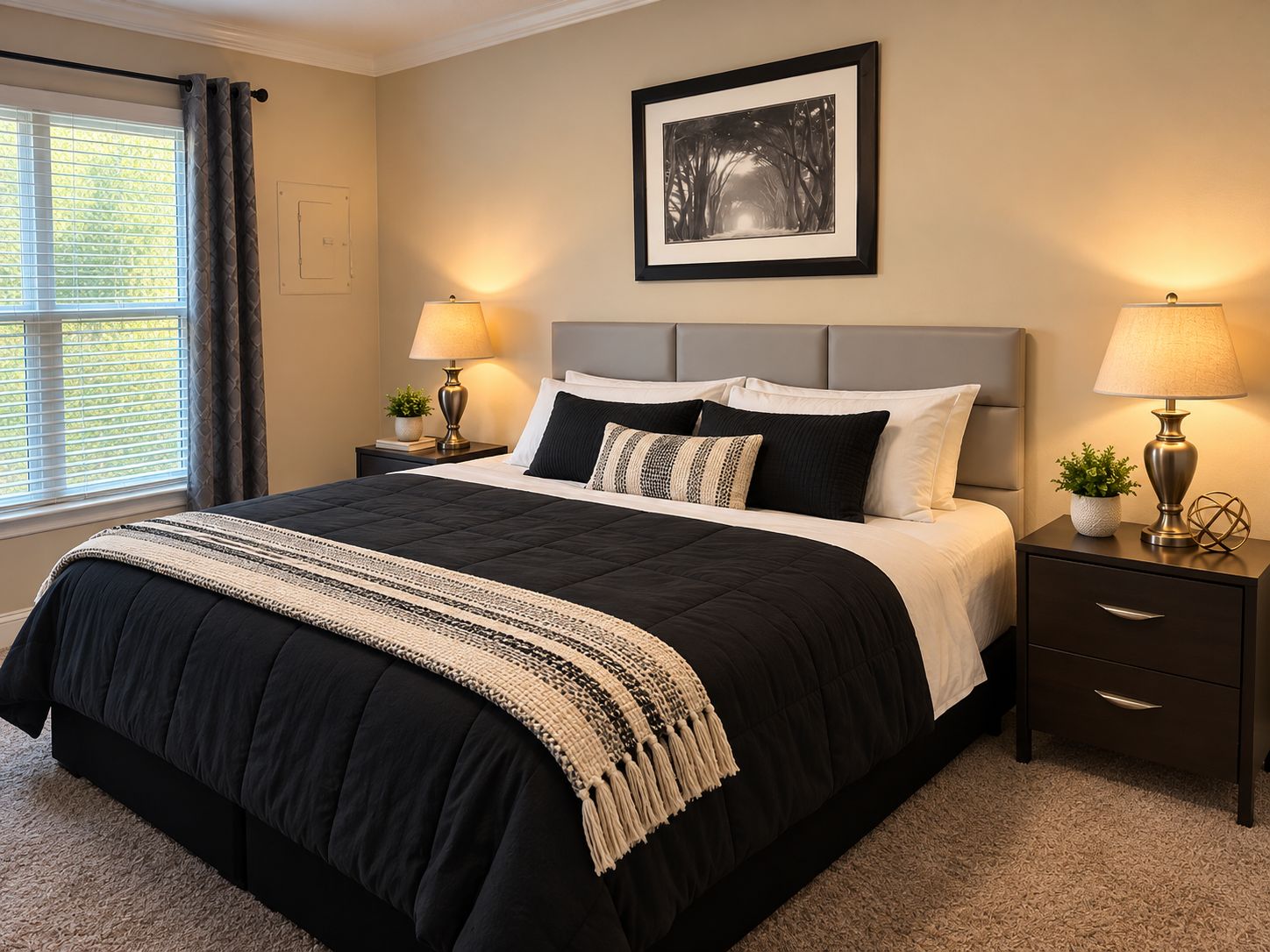 A bedroom with a large bed, two bedside tables with lamps, a framed picture on the wall, and a window with curtains.