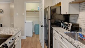 Una cocina con armarios blancos, un refrigerador de acero inoxidable, un tostador y un bote de basura.