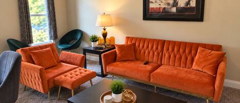 A living room with a sofa, two armchairs, a coffee table, a lamp, and a framed artwork on the wall.