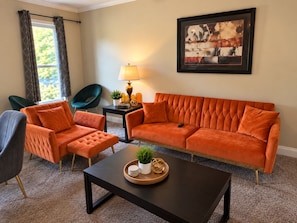 A living room with a sofa, two armchairs, a coffee table, a lamp, and a framed artwork on the wall. - The Durham Skybox (Durham)