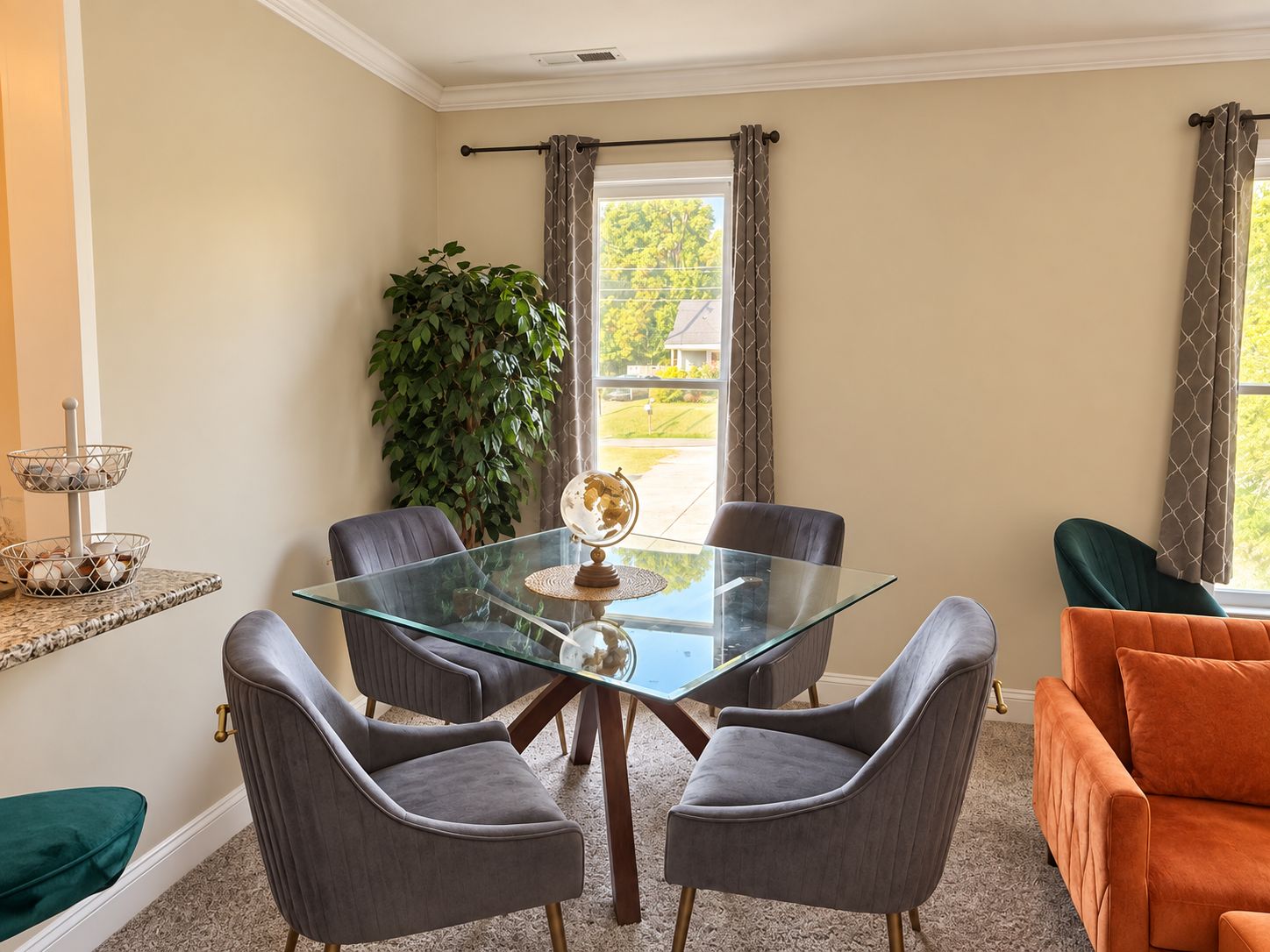 Un comedor con una mesa de vidrio, cuatro sillas grises, un globo terráqueo y una planta en maceta.