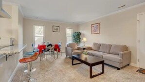 Una sala de estar moderna con un sofá color beige, una mesita de centro y un comedor con mantel rojo.
