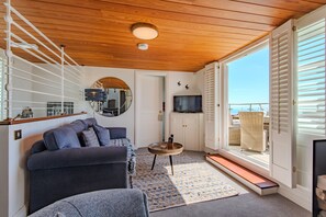 Una sala de estar con un sofá, una mesa de centro, un televisor y vistas a través de una puerta.