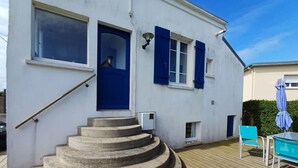 Een wit gebouw met blauwe luiken, een houten terras en een trap naar de ingang.