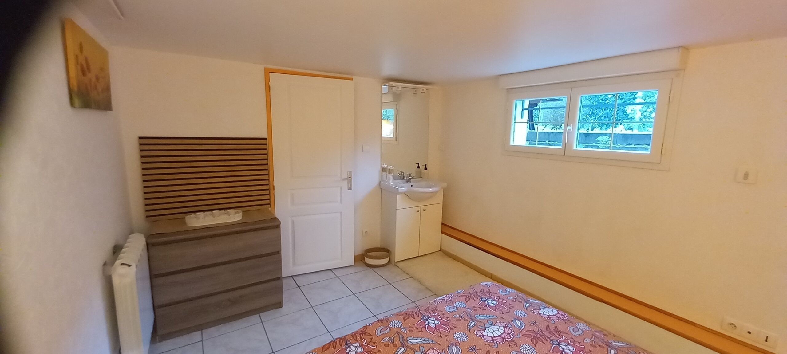 A bedroom with a bed, a wooden headboard, a window, a sink, and a door.