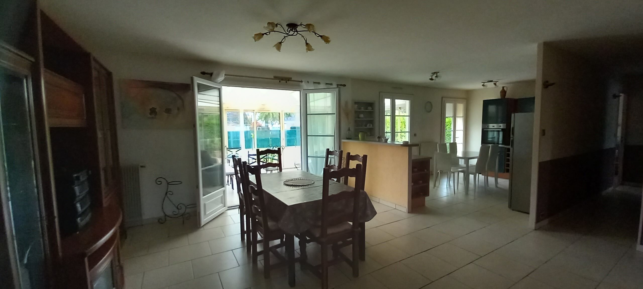 A spacious living area with a dining table, chairs, a kitchen area, and a sliding glass door leading to an outdoor space.