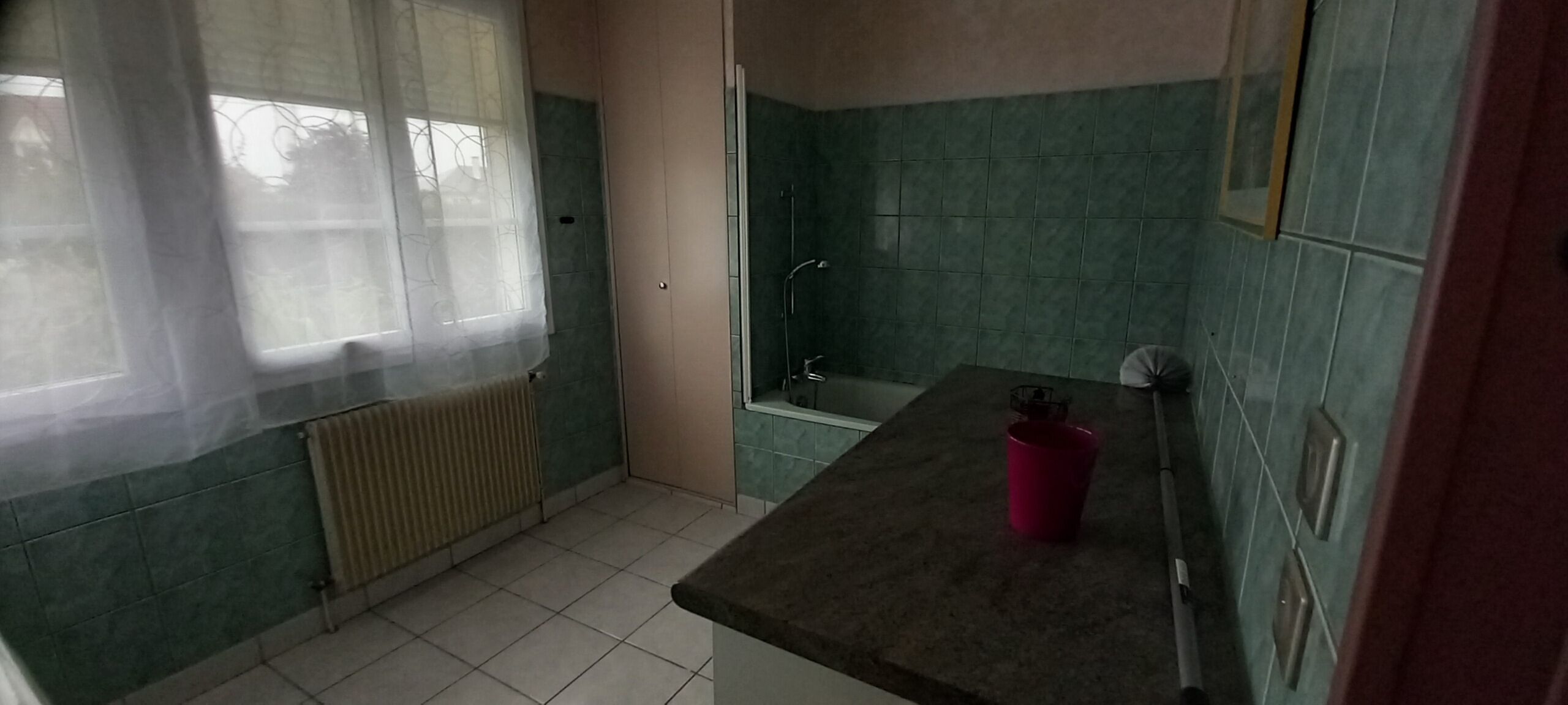 Un bagno piccolo con doccia, termosifone e finestra con tende.