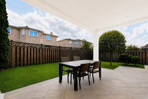 A patio area with a table and chairs, a wooden fence, and a lawn.