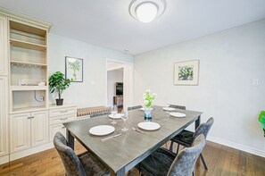 A dining area with a wooden table set for four, surrounded by chairs, with a bench and a cabinet with shelves.