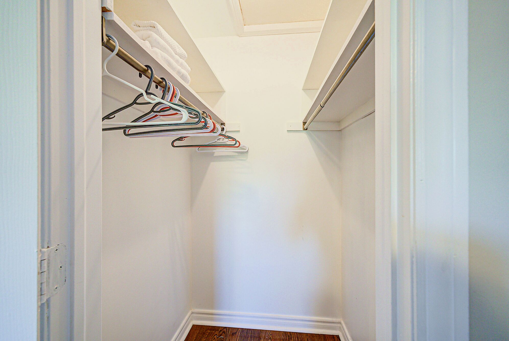 A narrow hallway with a white door at the end, leading to a room with a wooden floor.