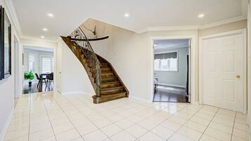 A spacious interior with a wooden staircase, tiled flooring, and a view of a dining area.