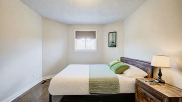 A bedroom with a bed, a nightstand, a lamp, a window, and a picture on the wall.