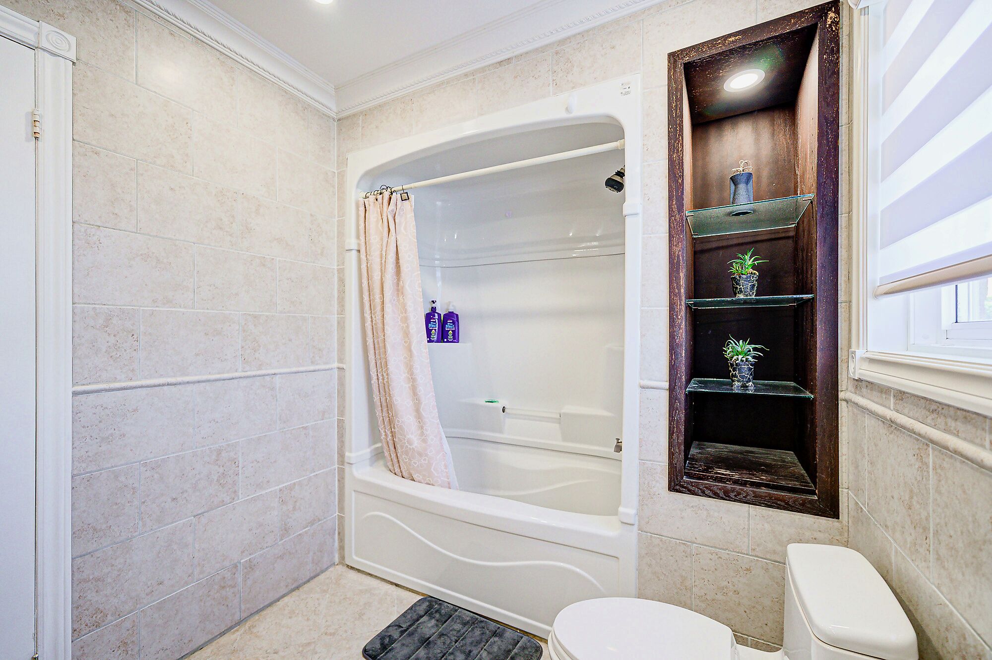 A bathroom with a bathtub, toilet, and a shelf with decorative items.