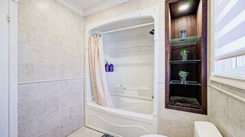 A bathroom with a bathtub, toilet, and a shelf with decorative items.