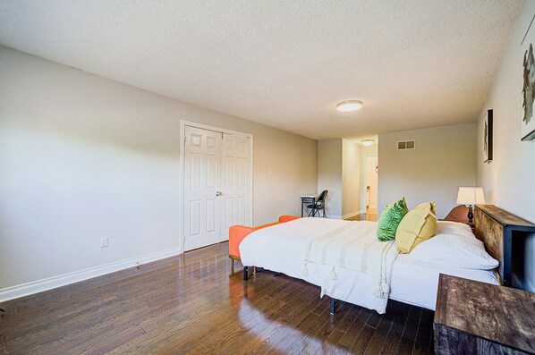 A bedroom with a bed, a chair, a desk, and a door.
