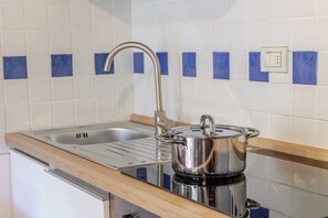 Eine Küche mit Spüle, einem Edelstahlkochtopf auf einem Feldoffener Herd und blauen Fliesen an der Wand.
