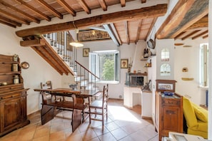 Eine rustikale Küche mit Holzbalken, einem Esstisch, Stühlen, einer Treppe und einem Fenster.