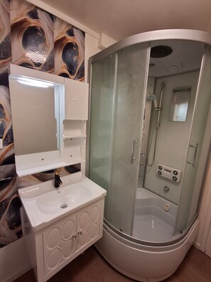 Ein Badezimmer mit Duschkabine, Waschbecken mit Spiegel und Schminktisch mit Dekorkabinetten.