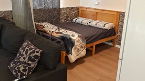 A room with a bed, a sofa, a curtain, and a refrigerator. - Charming Studio With Ocean Views in Auckland (Auckland)