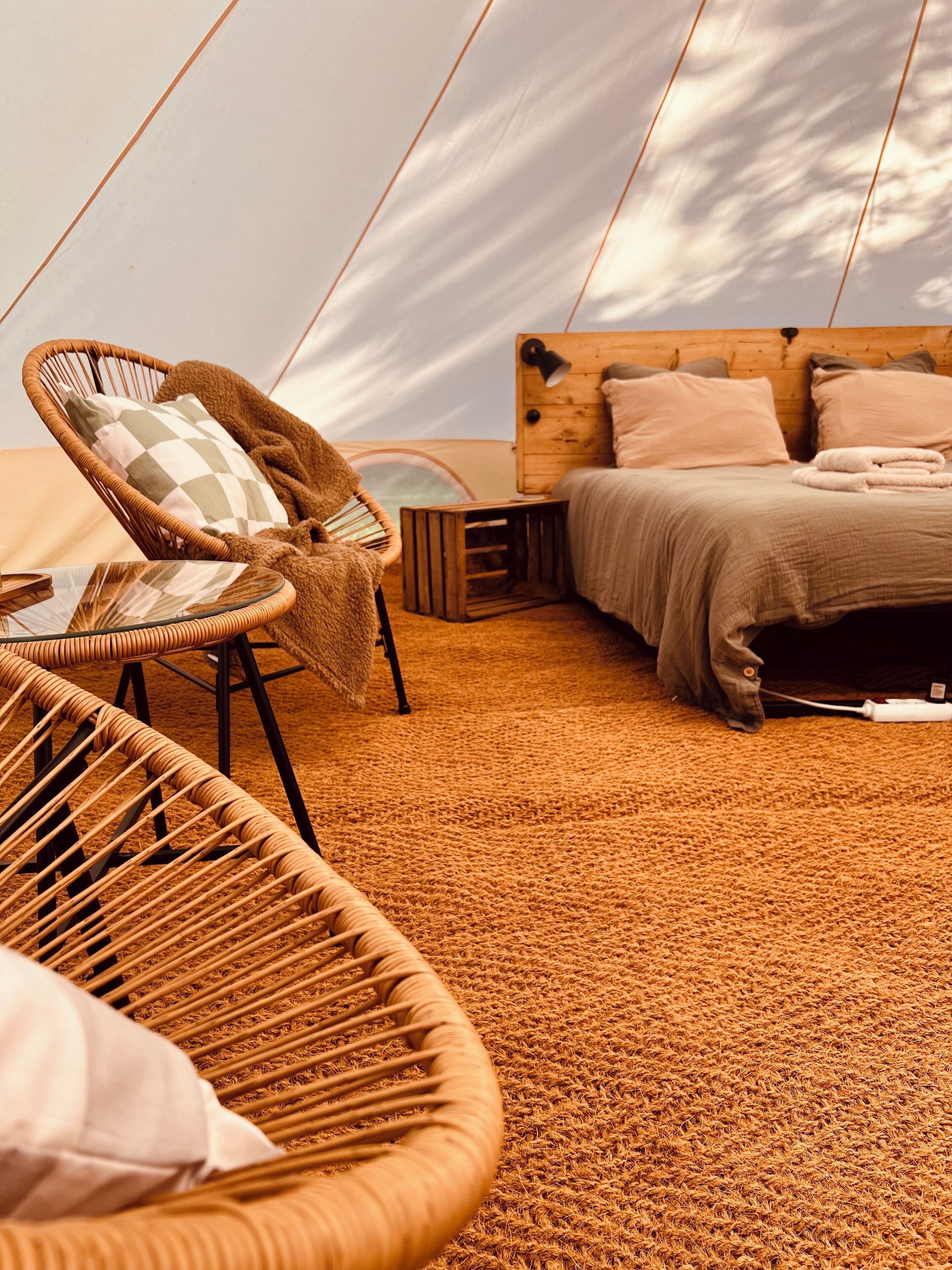 A tented accommodation with a bed, a wicker chair, and a small table.