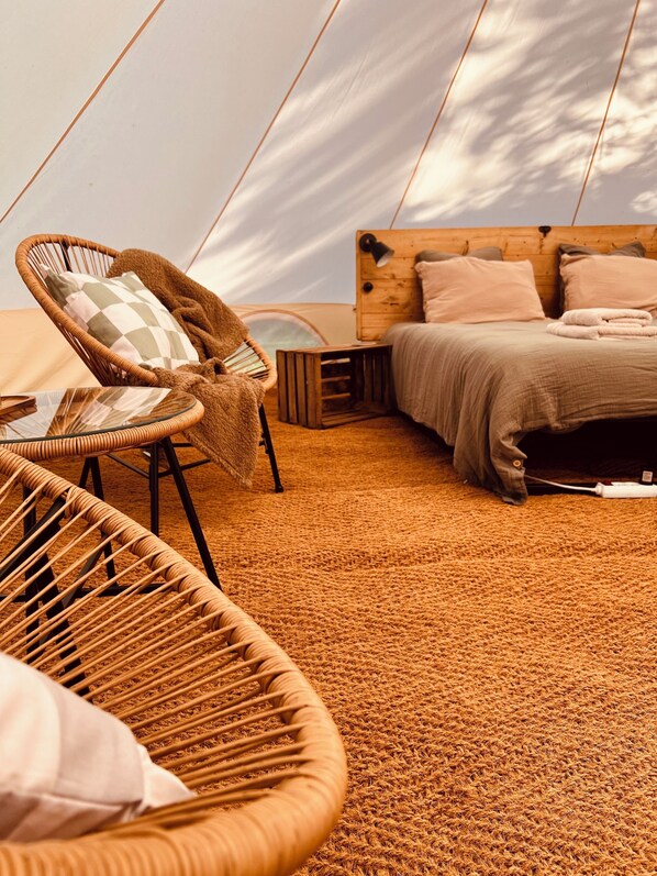 A tented accommodation with a bed, a wicker chair, and a small table.